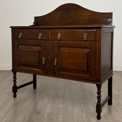 fig 2. An Edwardian dark oak sideboard featuring a shaped upstand gallery, two top drawers with brass drop handles, twin raised-panel cupboard doors, and front barley twist legs.