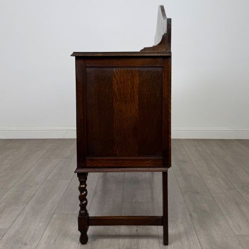 fig 3. An Edwardian dark oak sideboard featuring a shaped upstand gallery, two top drawers with brass drop handles, twin raised-panel cupboard doors, and front barley twist legs.