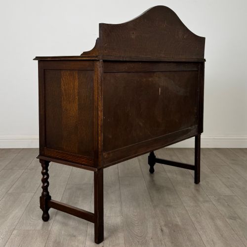 fig 4. An Edwardian dark oak sideboard featuring a shaped upstand gallery, two top drawers with brass drop handles, twin raised-panel cupboard doors, and front barley twist legs.
