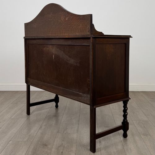 fig 6. An Edwardian dark oak sideboard featuring a shaped upstand gallery, two top drawers with brass drop handles, twin raised-panel cupboard doors, and front barley twist legs.