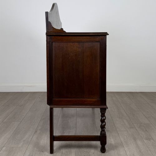 fig 7. An Edwardian dark oak sideboard featuring a shaped upstand gallery, two top drawers with brass drop handles, twin raised-panel cupboard doors, and front barley twist legs.