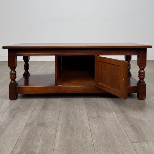 fig 1. A low rectangular warm brown oak coffee table featuring turned baluster legs, a lower shelf, and a central cupboard door decorated with carved linenfold panelling.