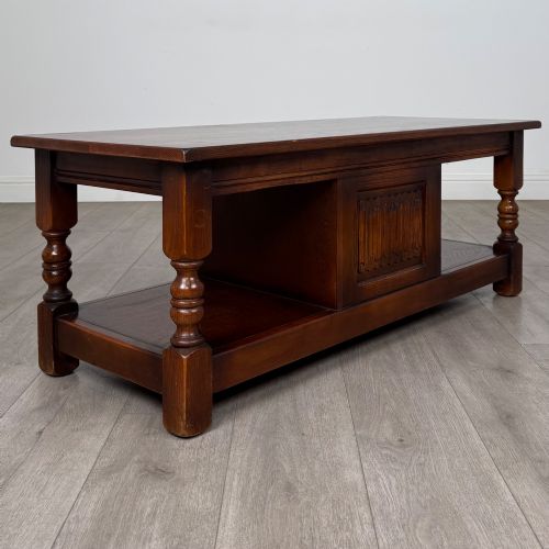 fig 4. A low rectangular warm brown oak coffee table featuring turned baluster legs, a lower shelf, and a central cupboard door decorated with carved linenfold panelling.