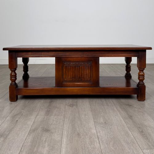 fig 5. A low rectangular warm brown oak coffee table featuring turned baluster legs, a lower shelf, and a central cupboard door decorated with carved linenfold panelling.