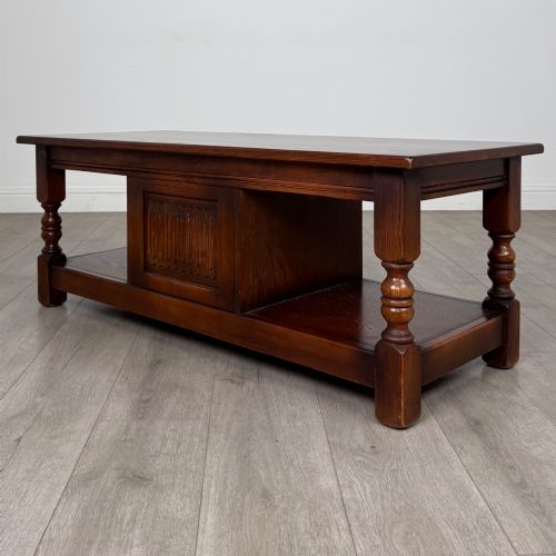 fig 6. A low rectangular warm brown oak coffee table featuring turned baluster legs, a lower shelf, and a central cupboard door decorated with carved linenfold panelling.