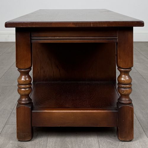 fig 7. A low rectangular warm brown oak coffee table featuring turned baluster legs, a lower shelf, and a central cupboard door decorated with carved linenfold panelling.