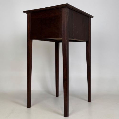 fig 3. An antique dark mahogany side table featuring two stacked drawers with circular handles, supported by tall tapered square legs.