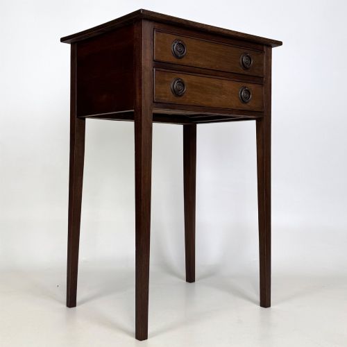fig 7. An antique dark mahogany side table featuring two stacked drawers with circular handles, supported by tall tapered square legs.