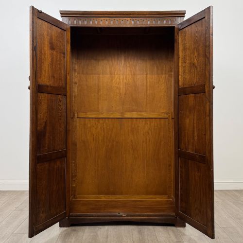 fig 1. A tall dark oak Edwardian two-door wardrobe featuring carved diamond panel details and decorative iron hinges.