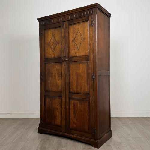 fig 2. A tall dark oak Edwardian two-door wardrobe featuring carved diamond panel details and decorative iron hinges.