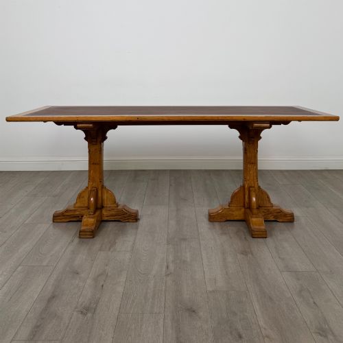 fig 1. A large twentieth-century Arts and Crafts oak library table with an inset brown leather writing top resting on dual pedestal trestle supports.