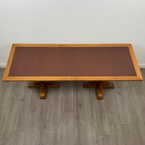 fig 3. A large twentieth-century Arts and Crafts oak library table with an inset brown leather writing top resting on dual pedestal trestle supports.