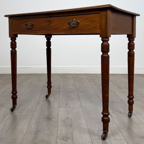 fig 1. A 19th-century Victorian golden oak writing table featuring a single frieze drawer with decorative brass handles and ring-turned legs on castors.