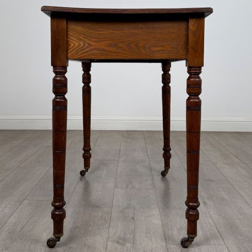 fig 2. A 19th-century Victorian golden oak writing table featuring a single frieze drawer with decorative brass handles and ring-turned legs on castors.