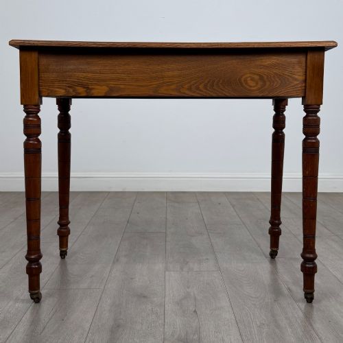 fig 4. A 19th-century Victorian golden oak writing table featuring a single frieze drawer with decorative brass handles and ring-turned legs on castors.