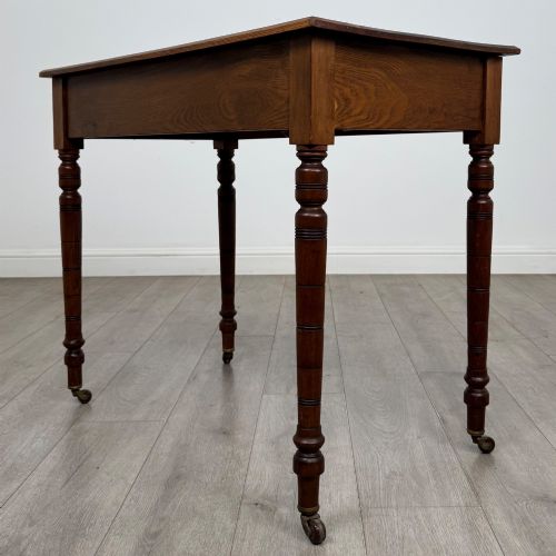 fig 5. A 19th-century Victorian golden oak writing table featuring a single frieze drawer with decorative brass handles and ring-turned legs on castors.