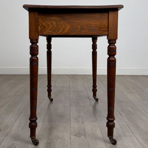 fig 6. A 19th-century Victorian golden oak writing table featuring a single frieze drawer with decorative brass handles and ring-turned legs on castors.