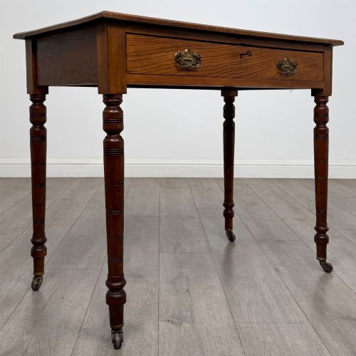 fig 7. A 19th-century Victorian golden oak writing table featuring a single frieze drawer with decorative brass handles and ring-turned legs on castors.