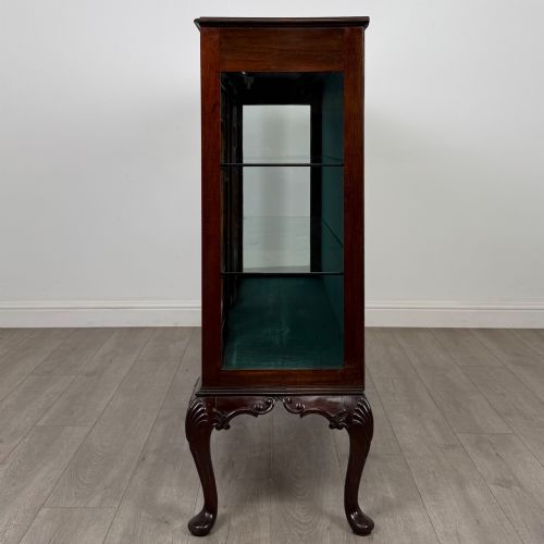 fig 3. An early twentieth-century mahogany display cabinet featuring three glazed doors with curved astragal glazing bars, a carved top frieze, green fabric interior, and cabriole legs.