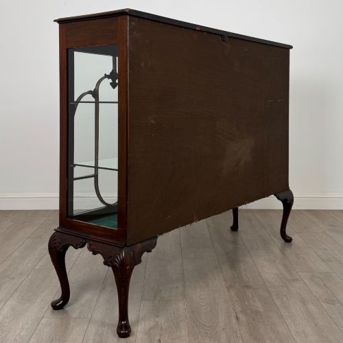 fig 4. An early twentieth-century mahogany display cabinet featuring three glazed doors with curved astragal glazing bars, a carved top frieze, green fabric interior, and cabriole legs.