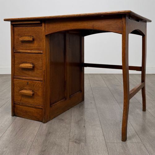 fig 1. An Edwardian single pedestal oak desk with three stacked drawers on the left, integrated wood pulls, and an open kneehole section supported by slim right-side legs.