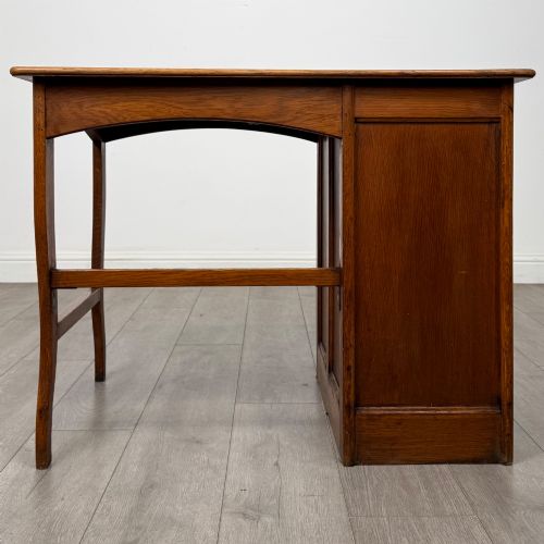 fig 4. An Edwardian single pedestal oak desk with three stacked drawers on the left, integrated wood pulls, and an open kneehole section supported by slim right-side legs.
