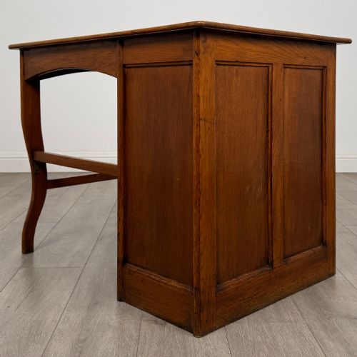 fig 5. An Edwardian single pedestal oak desk with three stacked drawers on the left, integrated wood pulls, and an open kneehole section supported by slim right-side legs.