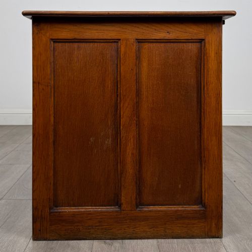 fig 6. An Edwardian single pedestal oak desk with three stacked drawers on the left, integrated wood pulls, and an open kneehole section supported by slim right-side legs.