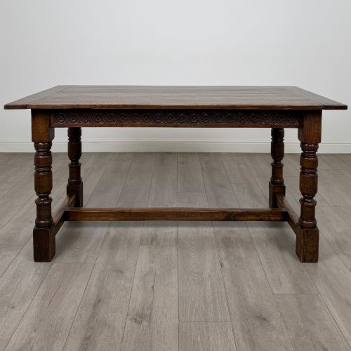 fig 1. A dark carved oak refectory dining table featuring a carved frieze apron, turned baluster legs, and an H-stretcher base on light timber flooring.