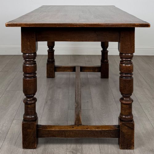fig 2. A dark carved oak refectory dining table featuring a carved frieze apron, turned baluster legs, and an H-stretcher base on light timber flooring.