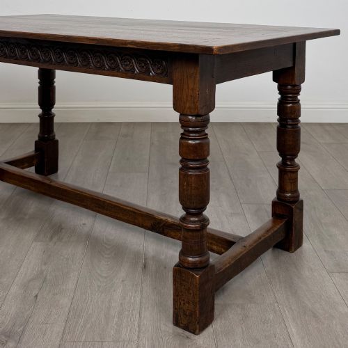 fig 4. A dark carved oak refectory dining table featuring a carved frieze apron, turned baluster legs, and an H-stretcher base on light timber flooring.