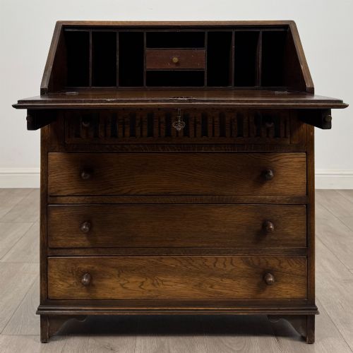 fig 1. A dark oak writing bureau with a slanted fall-front upper section featuring three carved linenfold panels above four drawers with turned wooden knob handles.