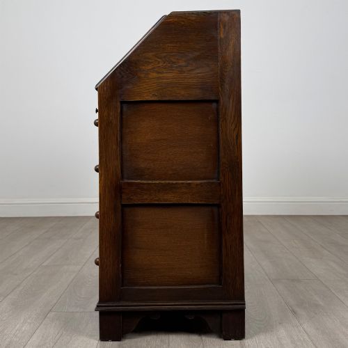 fig 3. A dark oak writing bureau with a slanted fall-front upper section featuring three carved linenfold panels above four drawers with turned wooden knob handles.
