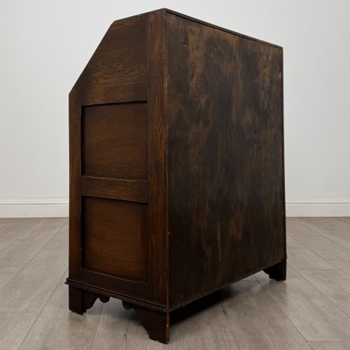 fig 4. A dark oak writing bureau with a slanted fall-front upper section featuring three carved linenfold panels above four drawers with turned wooden knob handles.