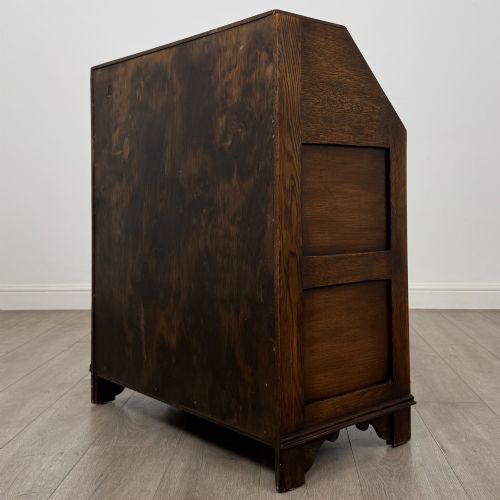 fig 6. A dark oak writing bureau with a slanted fall-front upper section featuring three carved linenfold panels above four drawers with turned wooden knob handles.