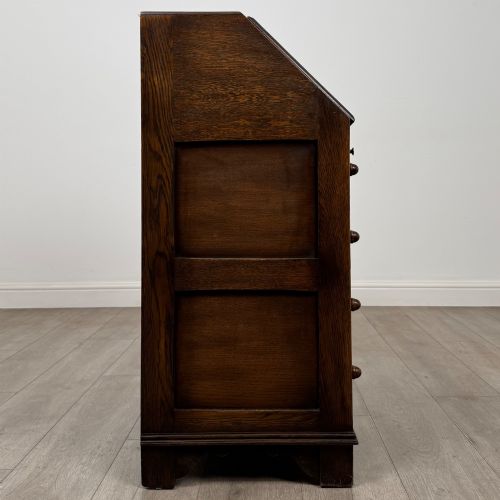 fig 7. A dark oak writing bureau with a slanted fall-front upper section featuring three carved linenfold panels above four drawers with turned wooden knob handles.
