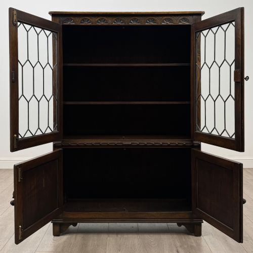 fig 1. A dark oak display cabinet featuring two upper leaded glass doors, lower cupboard doors carved with linenfold panels, and decorative metal hinges.
