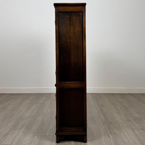 fig 3. A dark oak display cabinet featuring two upper leaded glass doors, lower cupboard doors carved with linenfold panels, and decorative metal hinges.