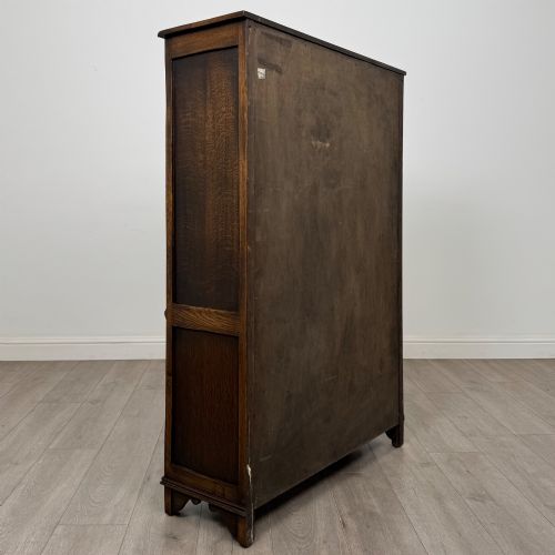 fig 4. A dark oak display cabinet featuring two upper leaded glass doors, lower cupboard doors carved with linenfold panels, and decorative metal hinges.