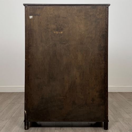 fig 5. A dark oak display cabinet featuring two upper leaded glass doors, lower cupboard doors carved with linenfold panels, and decorative metal hinges.