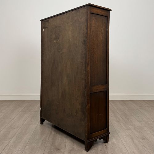 fig 6. A dark oak display cabinet featuring two upper leaded glass doors, lower cupboard doors carved with linenfold panels, and decorative metal hinges.