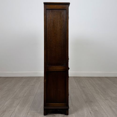 fig 7. A dark oak display cabinet featuring two upper leaded glass doors, lower cupboard doors carved with linenfold panels, and decorative metal hinges.