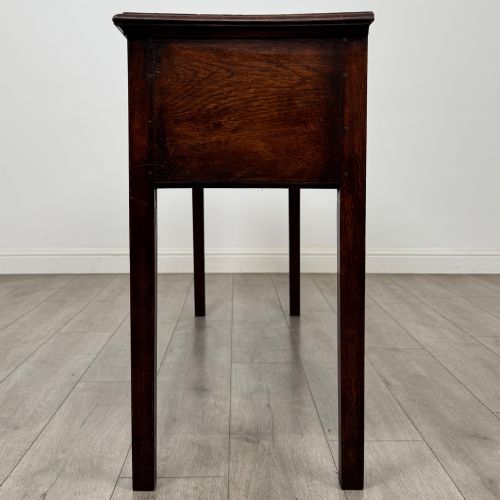 fig 2. An antique dark oak dresser base featuring three crossbanded drawers with brass drop handles and keyhole escutcheons, supported by four straight square legs.