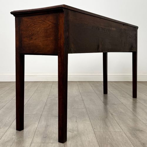 fig 3. An antique dark oak dresser base featuring three crossbanded drawers with brass drop handles and keyhole escutcheons, supported by four straight square legs.