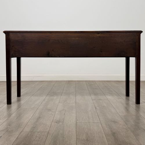 fig 4. An antique dark oak dresser base featuring three crossbanded drawers with brass drop handles and keyhole escutcheons, supported by four straight square legs.