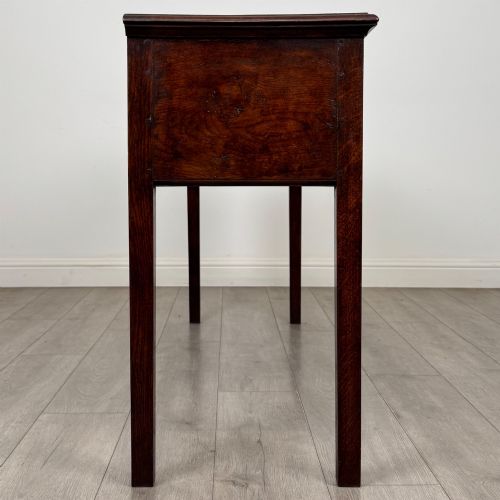 fig 6. An antique dark oak dresser base featuring three crossbanded drawers with brass drop handles and keyhole escutcheons, supported by four straight square legs.
