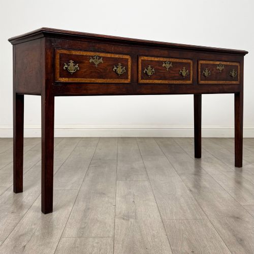 fig 7. An antique dark oak dresser base featuring three crossbanded drawers with brass drop handles and keyhole escutcheons, supported by four straight square legs.