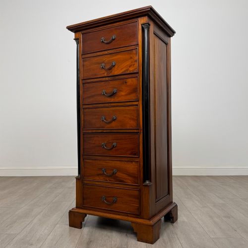 fig 1. A tall, narrow mahogany chest featuring seven drawers flanked by dark ebonised side columns on bracket feet.