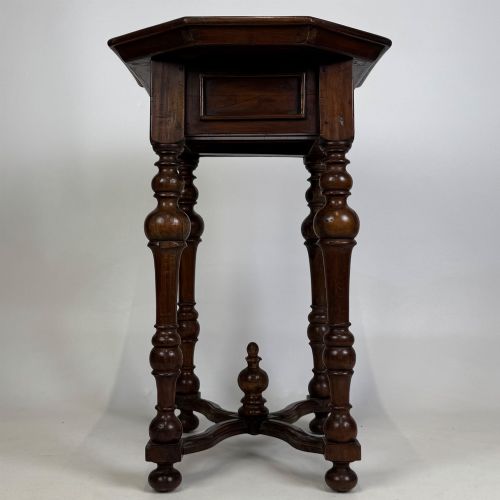 fig 2. A dark brown hardwood octagonal side table with turned legs, a single drawer with a brass pull, and an arched cross-stretcher featuring a central finial.