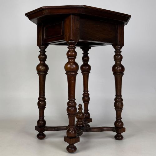 fig 3. A dark brown hardwood octagonal side table with turned legs, a single drawer with a brass pull, and an arched cross-stretcher featuring a central finial.